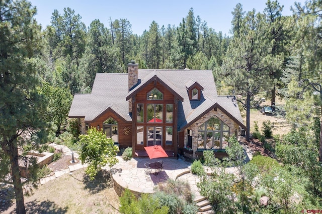 view of front of house featuring a patio area, a fire pit, a wooded view, and a chimney