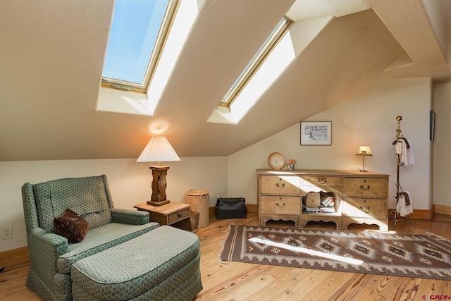 living area with vaulted ceiling with skylight, baseboards, and wood finished floors