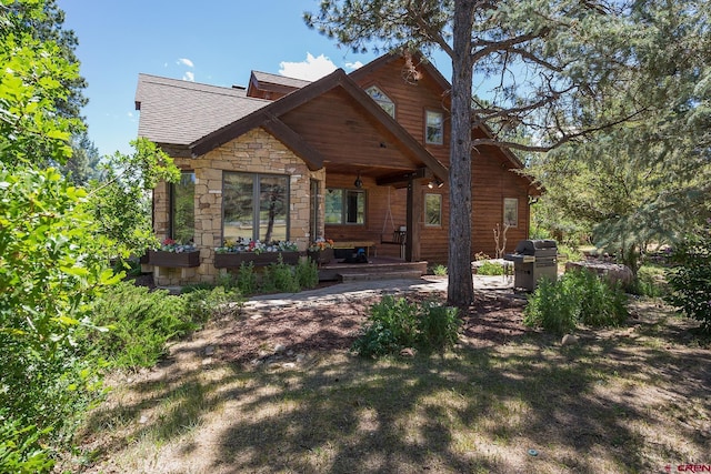 rear view of house with stone siding and a shingled roof