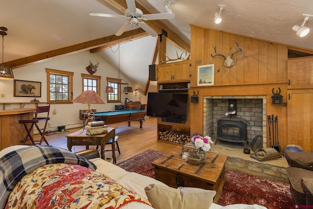 living room with vaulted ceiling with beams, ceiling fan, wood walls, light wood-style flooring, and a wood stove