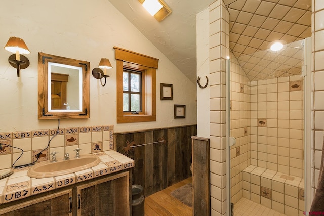 full bath with vanity, wood finished floors, lofted ceiling, a shower stall, and wainscoting