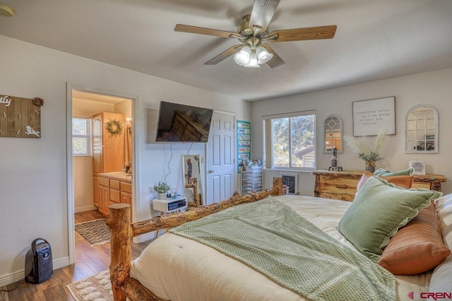 bedroom with a textured ceiling, ensuite bath, wood finished floors, baseboards, and ceiling fan