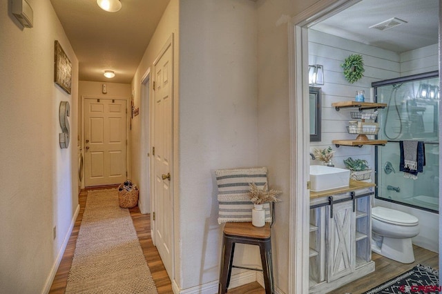 corridor featuring visible vents, a sink, baseboards, and wood finished floors