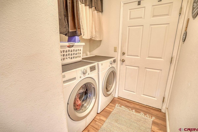 laundry room featuring washer and dryer, laundry area, a textured wall, and light wood finished floors