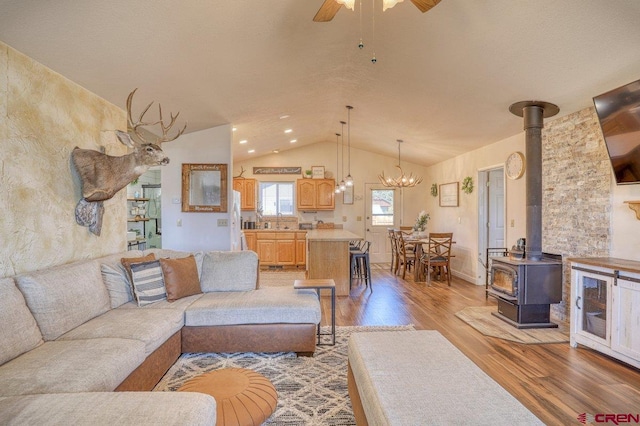 living room with ceiling fan with notable chandelier, lofted ceiling, a wood stove, and light wood-style floors