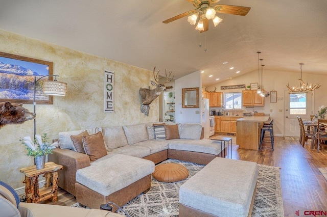 living area with baseboards, lofted ceiling, light wood-style flooring, recessed lighting, and ceiling fan with notable chandelier