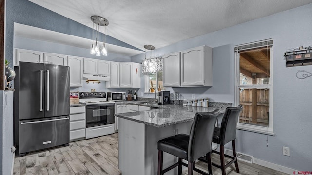 kitchen with under cabinet range hood, vaulted ceiling, a peninsula, white cabinets, and stainless steel appliances