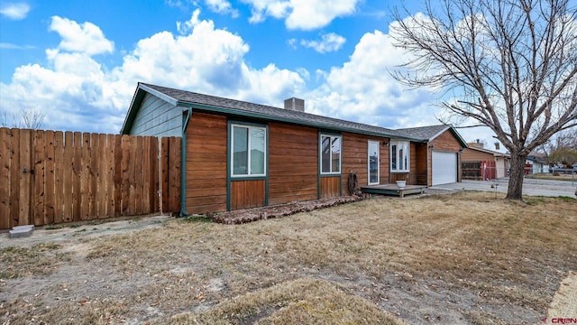 view of front facade featuring driveway, a chimney, an attached garage, and fence