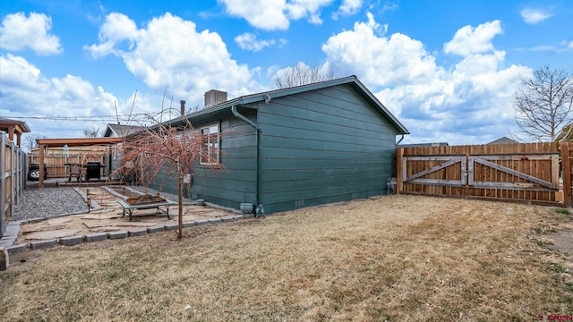 view of side of property with a lawn, a gate, fence, a fire pit, and a patio area