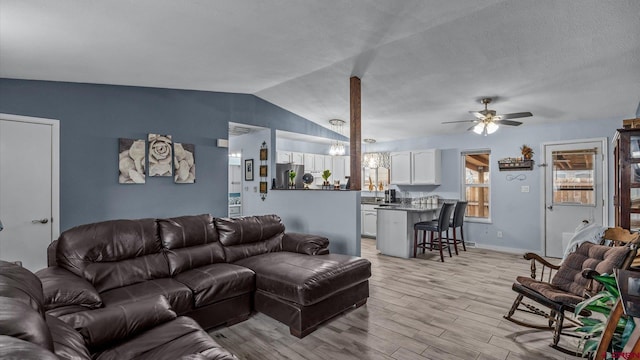 living area featuring baseboards, light wood-style flooring, ceiling fan, vaulted ceiling, and a textured ceiling