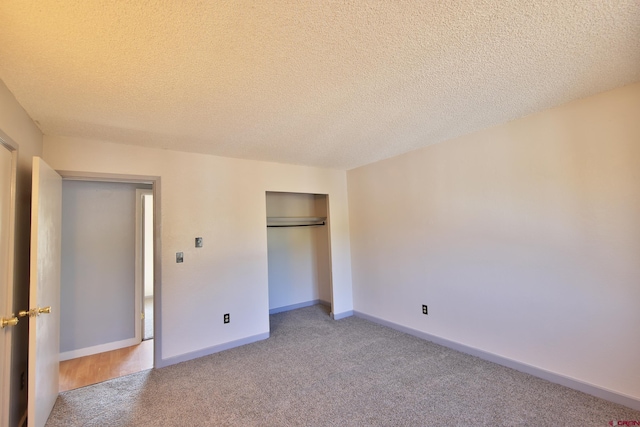 unfurnished bedroom featuring a closet, light colored carpet, a textured ceiling, and baseboards