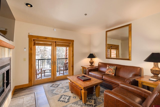 living area featuring a tiled fireplace, light wood-style flooring, french doors, and baseboards