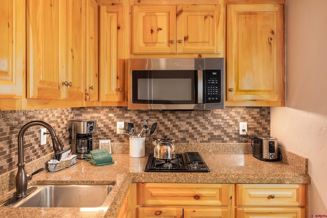 kitchen with light brown cabinetry, decorative backsplash, a sink, black gas cooktop, and stainless steel microwave