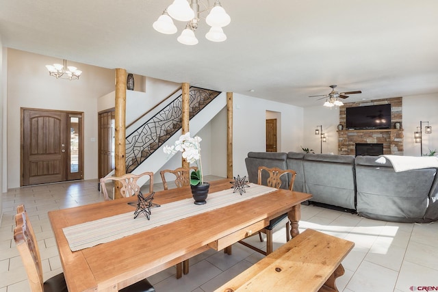 dining space featuring light tile patterned floors, a fireplace, stairs, and ceiling fan with notable chandelier