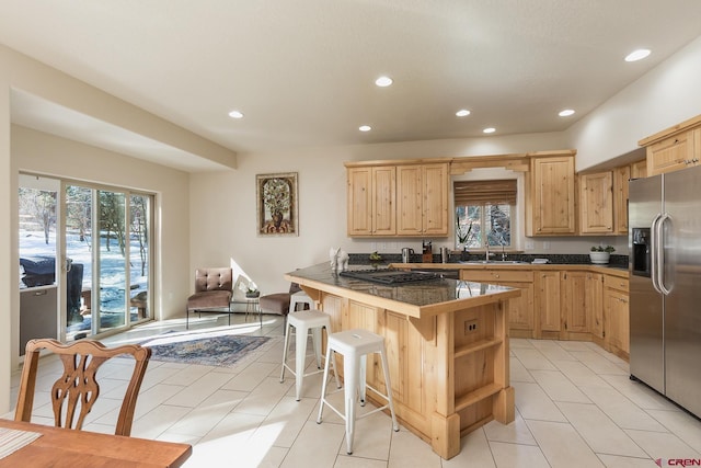 kitchen with a breakfast bar, light brown cabinets, stainless steel fridge, a peninsula, and a healthy amount of sunlight