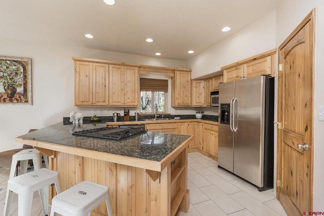 kitchen featuring light brown cabinets, tile counters, a kitchen breakfast bar, stainless steel appliances, and a sink