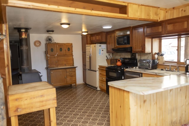 kitchen with black appliances, a sink, a peninsula, exhaust hood, and light countertops