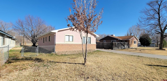 view of property exterior with a yard, fence, brick siding, and stucco siding