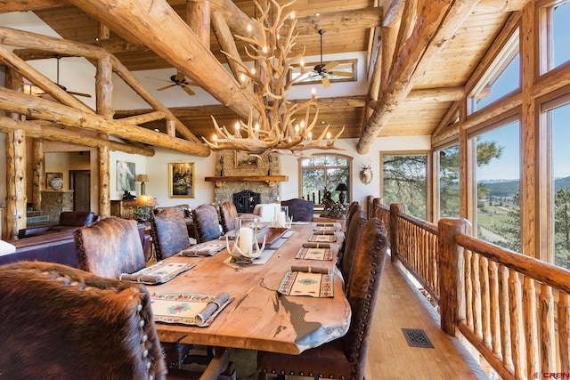 dining space with visible vents, beamed ceiling, light wood-type flooring, a stone fireplace, and high vaulted ceiling