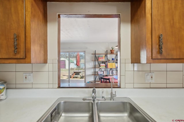 kitchen with light countertops, brown cabinetry, backsplash, and a sink