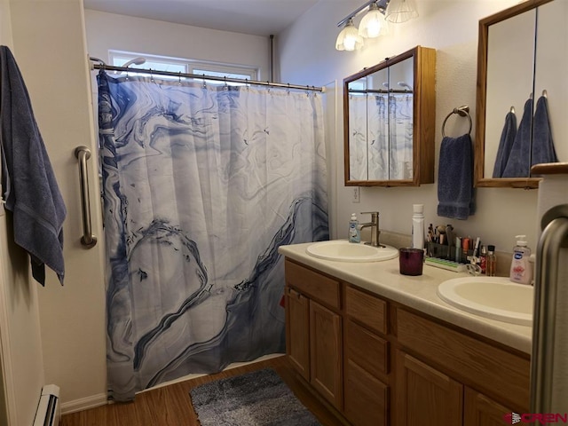 bathroom featuring double vanity, baseboard heating, wood finished floors, and a sink