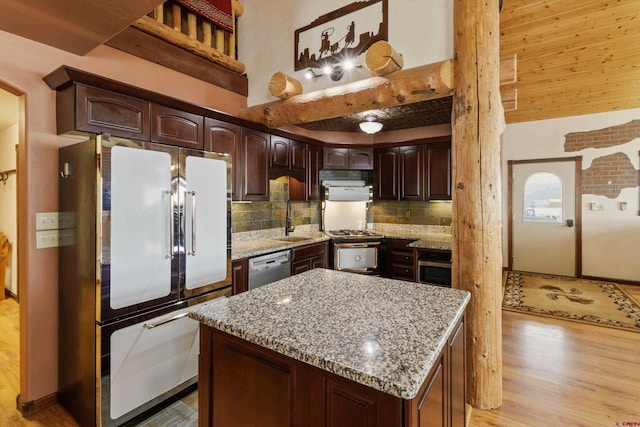 kitchen with a sink, tasteful backsplash, light wood-style floors, appliances with stainless steel finishes, and a towering ceiling