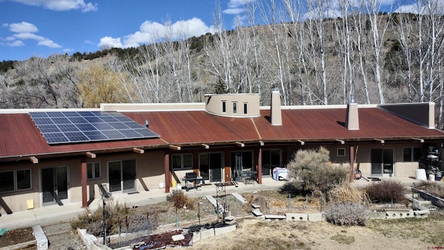 rear view of property featuring a patio area, a wooded view, roof mounted solar panels, and metal roof