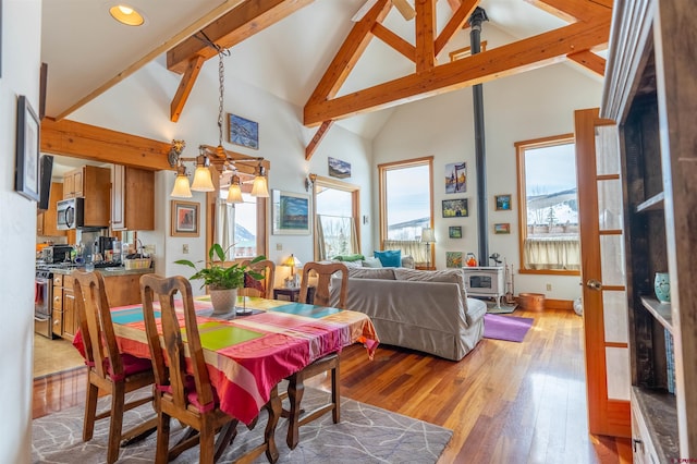 dining space with beamed ceiling, light wood-style floors, a chandelier, and a wood stove