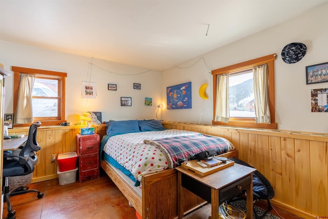 bedroom featuring wooden walls, multiple windows, and a wainscoted wall