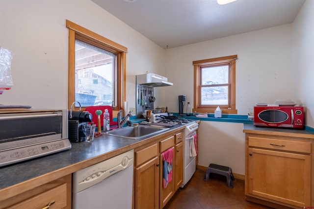 kitchen with white appliances, dark countertops, under cabinet range hood, and a sink