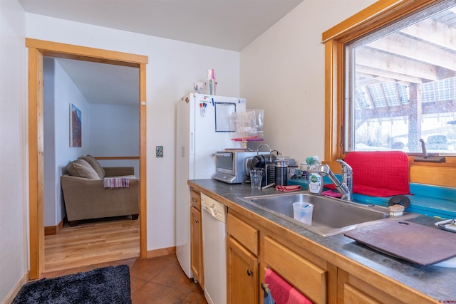 kitchen featuring dark countertops, baseboards, light tile patterned floors, white dishwasher, and a sink