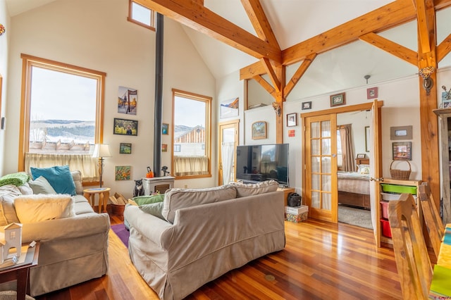 living room with beam ceiling, french doors, a wood stove, wood finished floors, and high vaulted ceiling