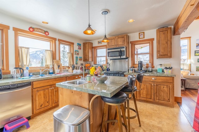 kitchen with brown cabinetry, a center island with sink, appliances with stainless steel finishes, and a sink