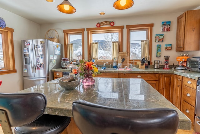 kitchen with tile countertops, a breakfast bar area, stainless steel refrigerator with ice dispenser, brown cabinetry, and a sink