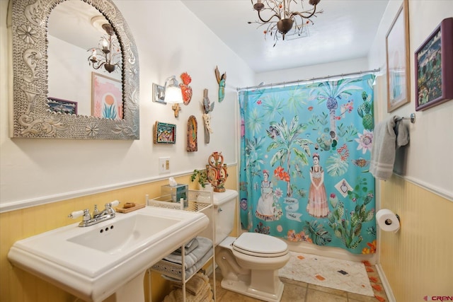 bathroom featuring tile patterned floors, a wainscoted wall, toilet, shower / bath combo, and a sink