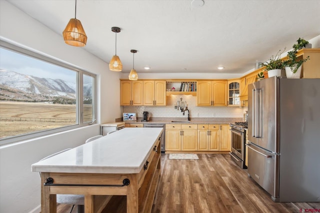 kitchen with light brown cabinets, light countertops, wood finished floors, stainless steel appliances, and a sink