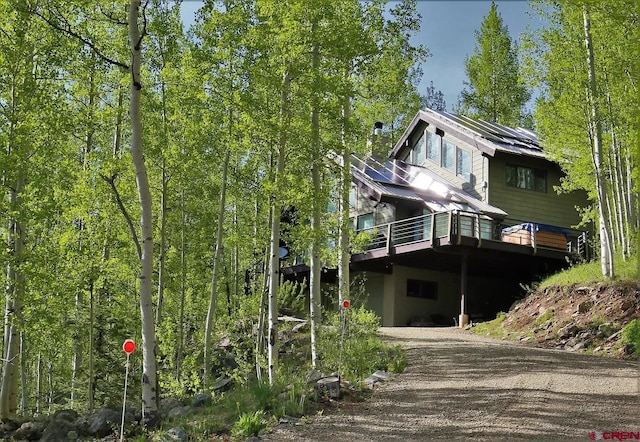 back of property with solar panels, a deck, and dirt driveway