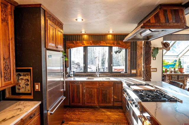 kitchen featuring premium range hood, high quality appliances, light stone counters, a sink, and dark wood finished floors