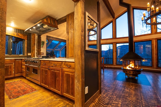 kitchen with double oven range, wood finished floors, brown cabinetry, island range hood, and a wood stove