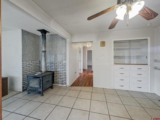 interior space with light tile patterned flooring, a wood stove, and a ceiling fan