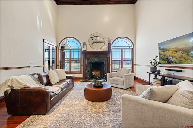 living room featuring a towering ceiling, wood finished floors, a fireplace, and crown molding