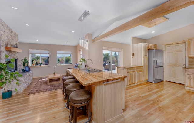 kitchen featuring light brown cabinets, a breakfast bar, a fireplace, a sink, and refrigerator with ice dispenser