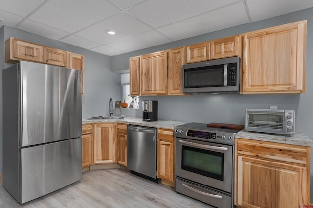 kitchen featuring a toaster, a drop ceiling, a sink, appliances with stainless steel finishes, and light wood-type flooring