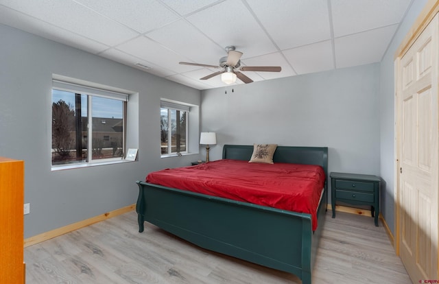 bedroom featuring visible vents, baseboards, a drop ceiling, wood finished floors, and a ceiling fan