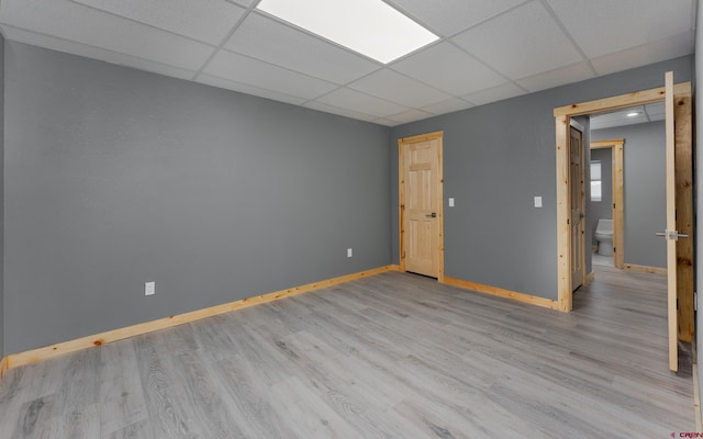 empty room with light wood-style flooring, a paneled ceiling, and baseboards