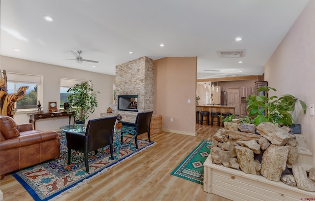 living area with a ceiling fan, wood finished floors, baseboards, recessed lighting, and a multi sided fireplace