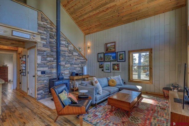 living area featuring wood walls, wooden ceiling, a wood stove, high vaulted ceiling, and wood-type flooring