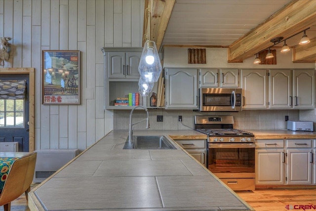 kitchen with beam ceiling, a sink, decorative backsplash, light countertops, and appliances with stainless steel finishes