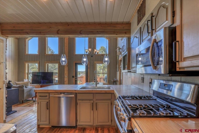 kitchen with tile countertops, stainless steel appliances, beamed ceiling, and a sink