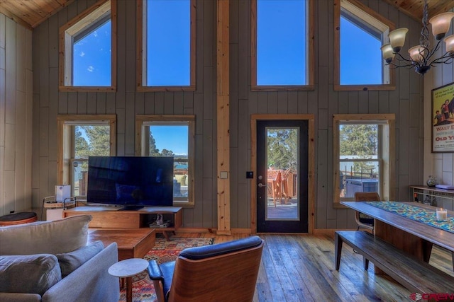 living area featuring a chandelier, wooden walls, a towering ceiling, and hardwood / wood-style flooring